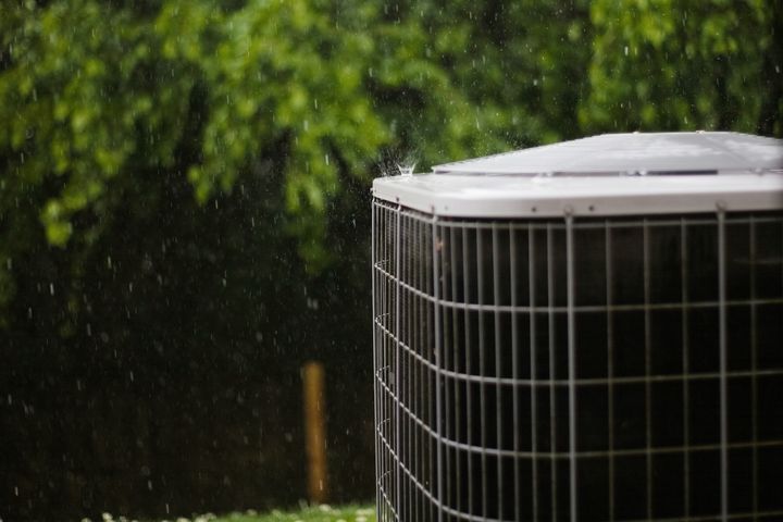 A central air conditioning condenser outside a house in the rain